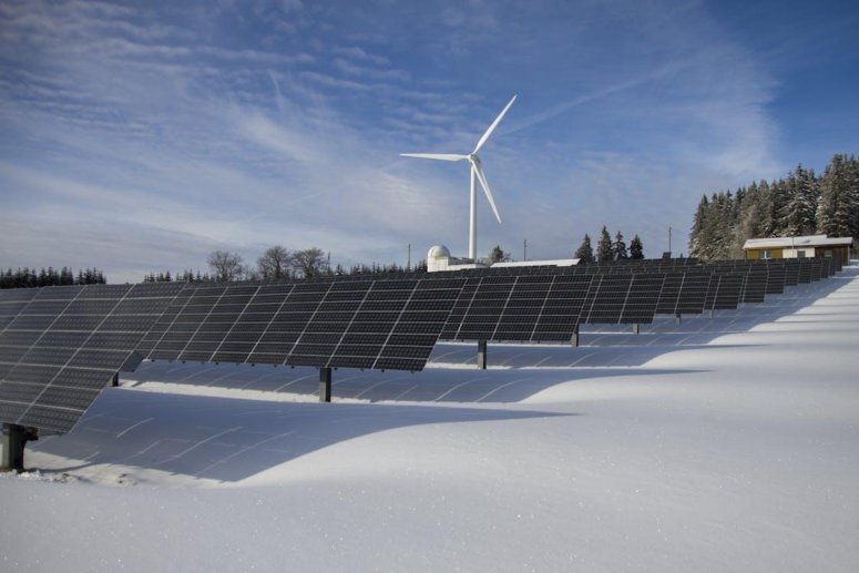 A series of solar panels lined up along with a windmill to produce renewable energy